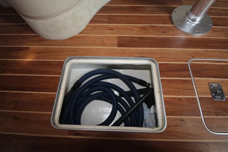 An open floor compartment with a coiled hose on a wooden deck.