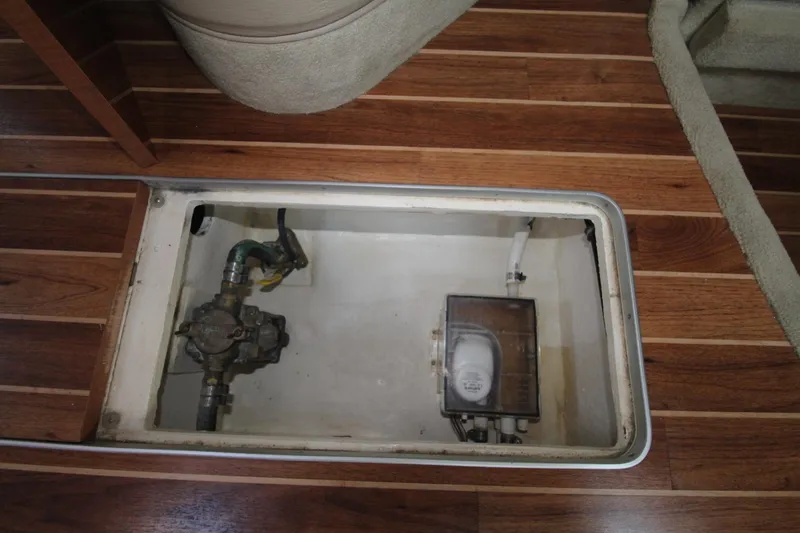 An open compartment in a boat's floor reveals plumbing and an electrical device.
