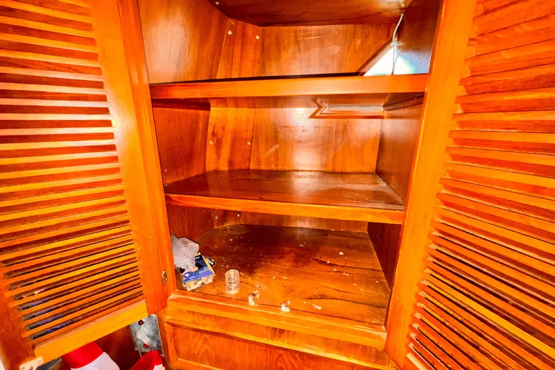 Empty wooden cabinet with open louvered doors, showing shelves and scattered items.
