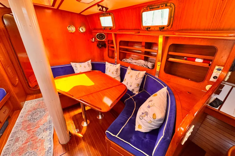 Cozy 1982 Kelly Peterson 46 yacht interior with wooden dining area and blue cushioned seating.