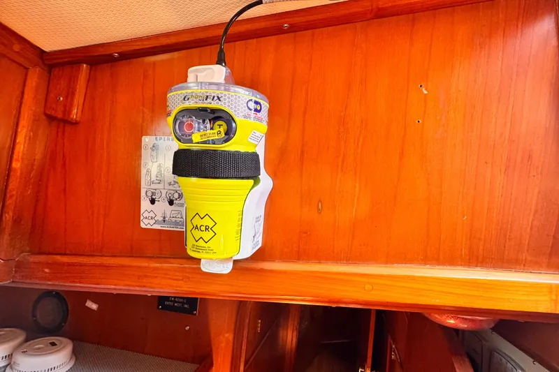 Yellow ACR EPIRB mounted on wooden panel inside 1982 Kelly Peterson 46 yacht.