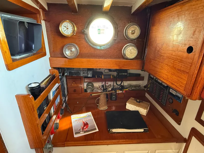 Interior of 1932 Fellows & Stewart Yawl with wooden desk, nautical instruments, and porthole.