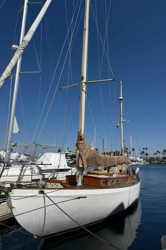 Historic 1932 Fellows & Stewart Yawl docked at marina under clear blue sky.