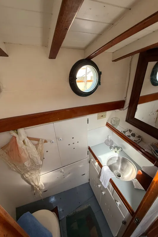 Interior of 1932 Fellows & Stewart Yawl, featuring a compact bathroom with porthole and wooden accents.