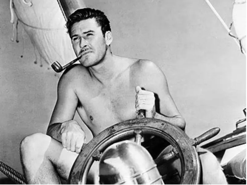 Shirtless man steering 1932 Fellows & Stewart Yawl, smoking pipe, vintage sailing scene.