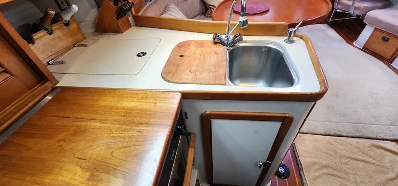 Interior of 1995 Catalina 42 MkII yacht, featuring a compact kitchen with sink and wooden cabinetry.