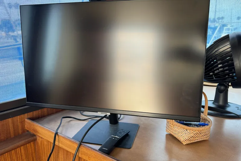 Samsung monitor and remote on a wooden desk inside a 1983 Hatteras 36 Convertible boat.