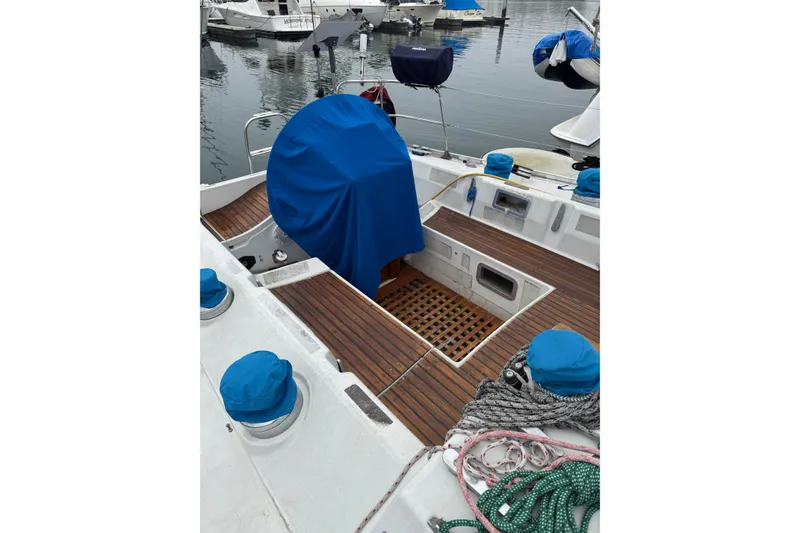 1985 Beneteau First 38 sailboat deck with blue covers and ropes in marina.