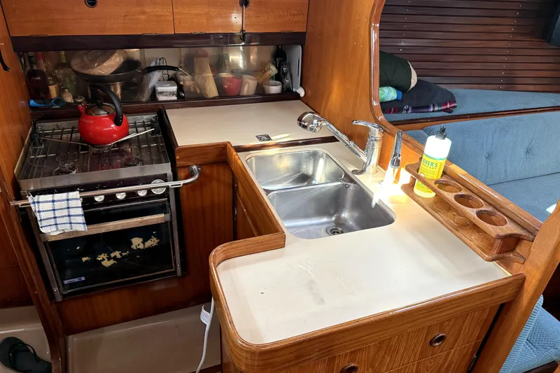 1985 Beneteau First 38 yacht kitchen with stove, sink, and wooden cabinetry.