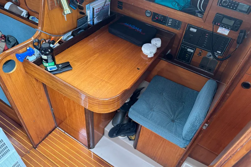 Navigation station inside a 1985 Beneteau First 38 sailboat, featuring wooden desk and blue cushioned seat.