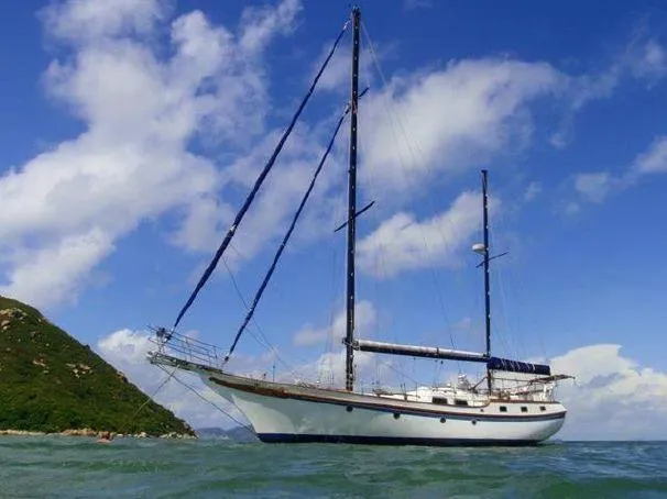 Sailing yacht Vagabond 47 from 1986 on calm waters near a lush island.