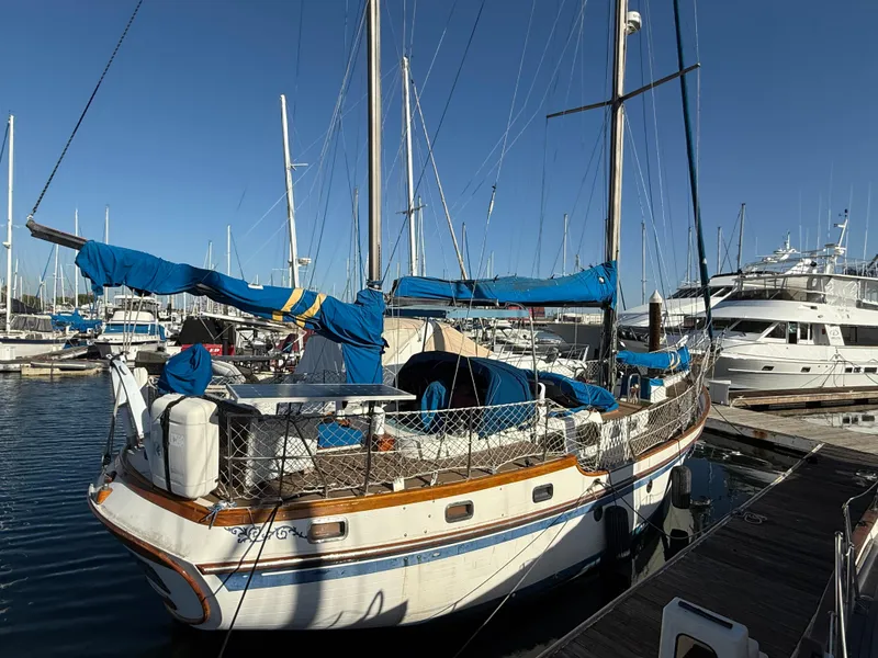 1986 Vagabond 47 sailboat docked in marina, surrounded by other boats under clear blue sky.