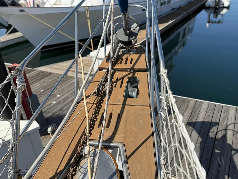 Bow of 1986 Vagabond 47 sailboat docked at marina, featuring wooden deck and anchor chain.
