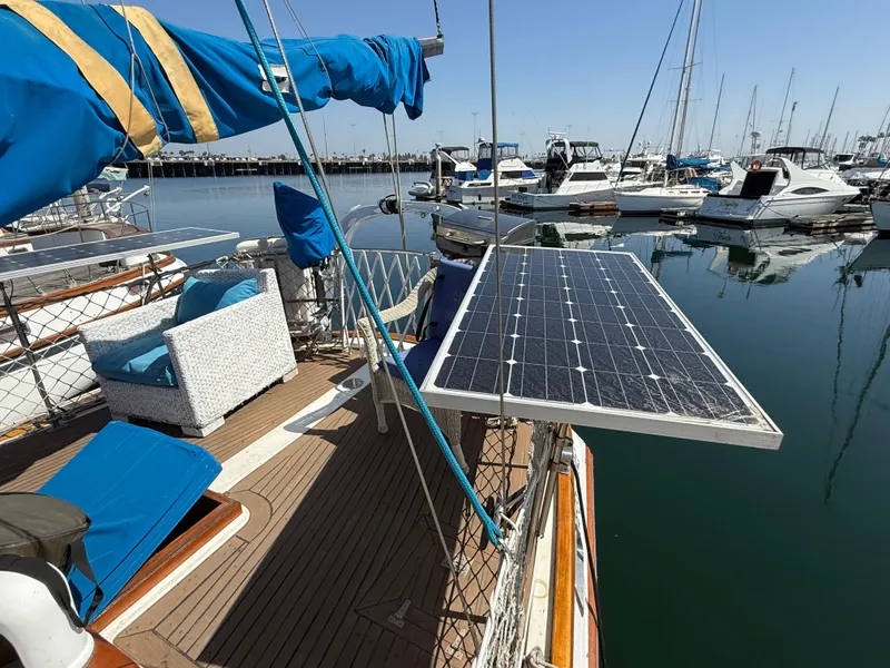 Sailboat Vagabond 47 (1986) with solar panels and seating, docked in a marina.