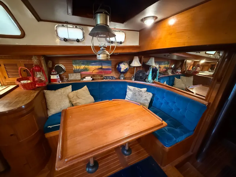 Luxurious 1986 Vagabond 47 yacht interior with blue cushioned seating and wooden table.