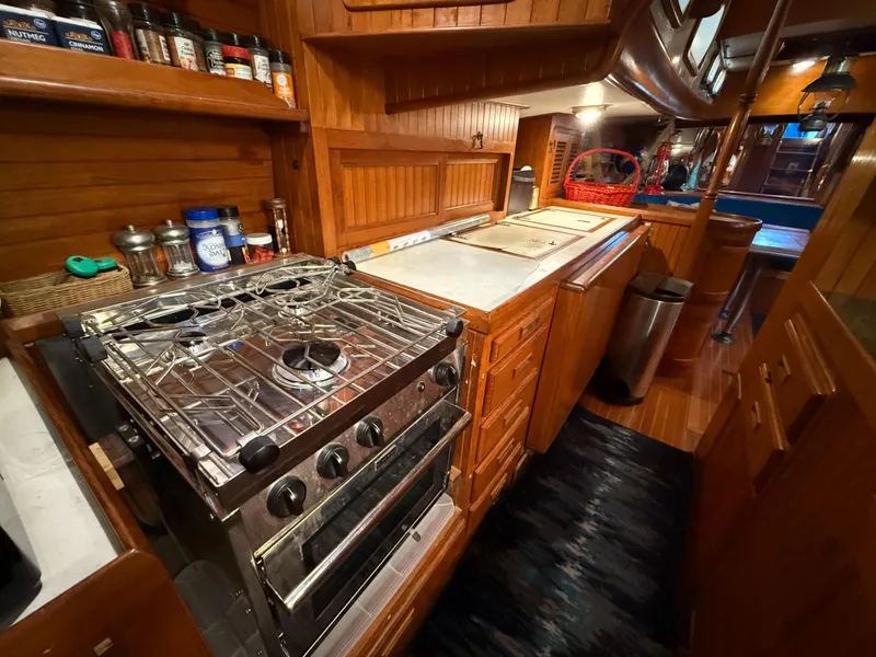 1986 Vagabond 47 yacht kitchen with wooden cabinetry, stove, and spice rack.