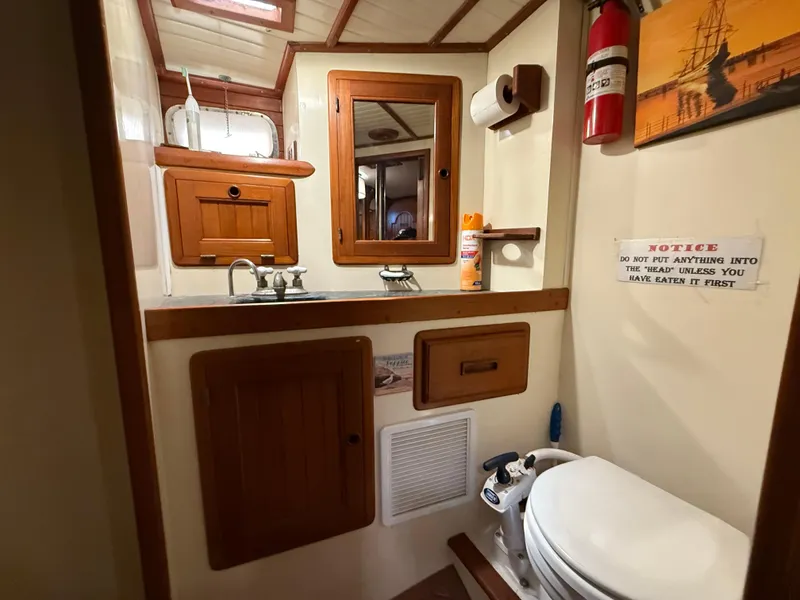 1986 Vagabond 47 yacht bathroom with wooden cabinets, sink, toilet, and fire extinguisher.