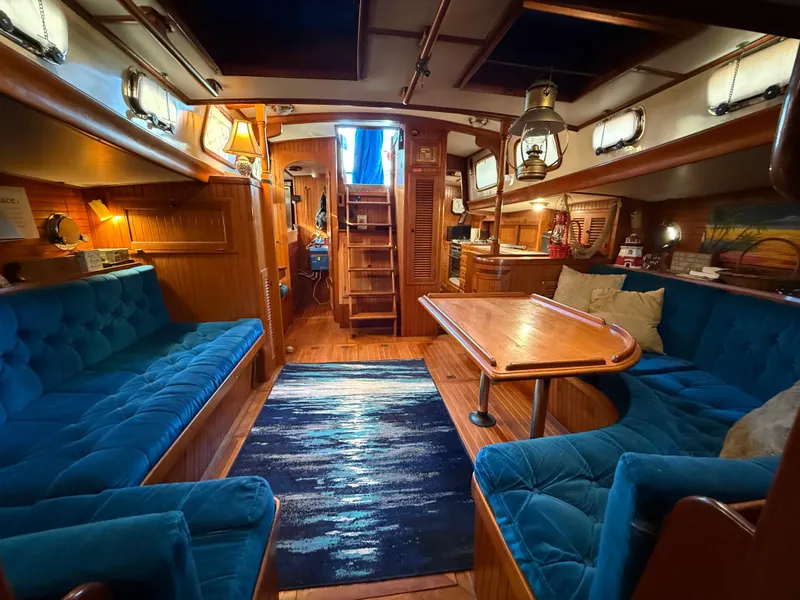 Cozy 1986 Vagabond 47 yacht interior with blue seating, wooden table, and nautical decor.