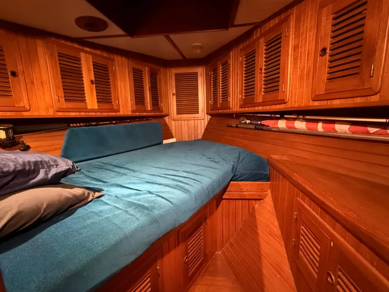 Cozy cabin interior of 1986 Vagabond 47 sailboat with wooden paneling and blue bedding.