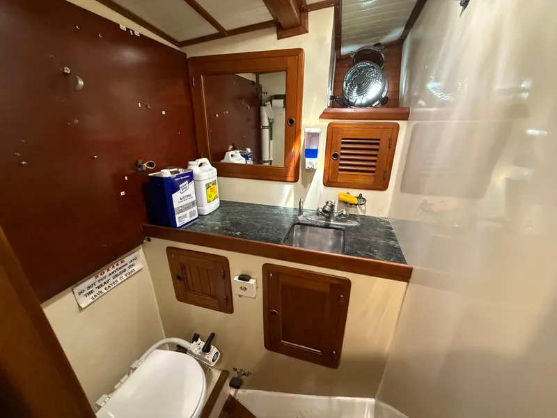 1986 Vagabond 47 yacht bathroom with wooden cabinetry, sink, and marine toilet.