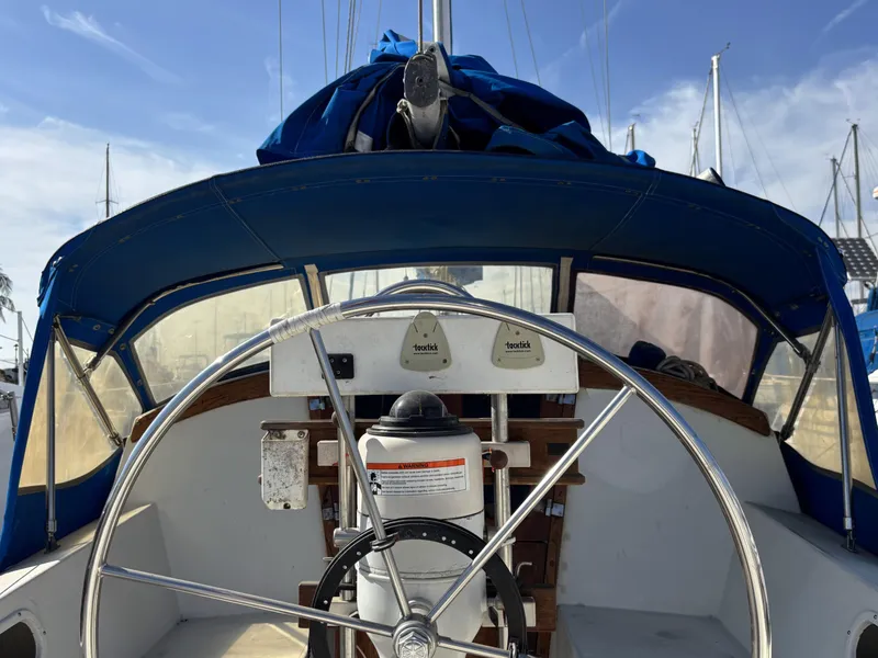 Cockpit of a 1985 Newport 30 sailboat with blue canopy and steering wheel.