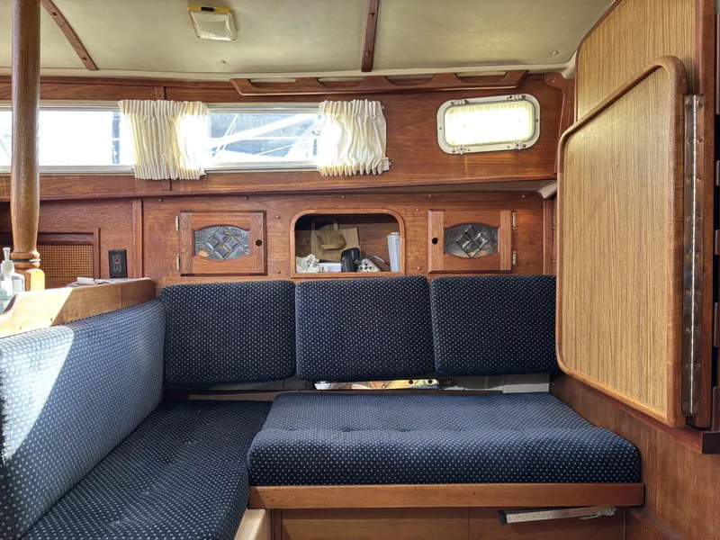 Interior of a 1985 Newport 30 sailboat with wooden cabinetry and blue cushioned seating.