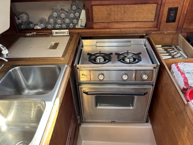 Compact kitchen in a 1985 Newport 30 yacht with stove, sink, and storage.
