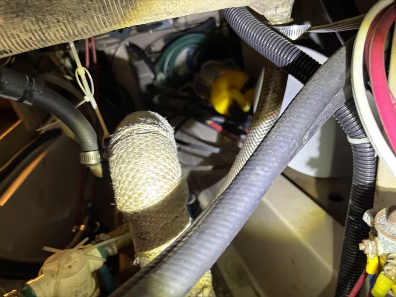 Engine compartment of a 1985 Newport 30 sailboat with various hoses and wiring.