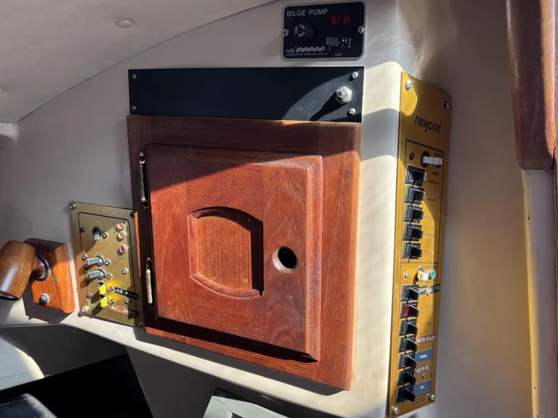 Control panel of a 1985 Newport 30 sailboat with switches and wooden cabinet.