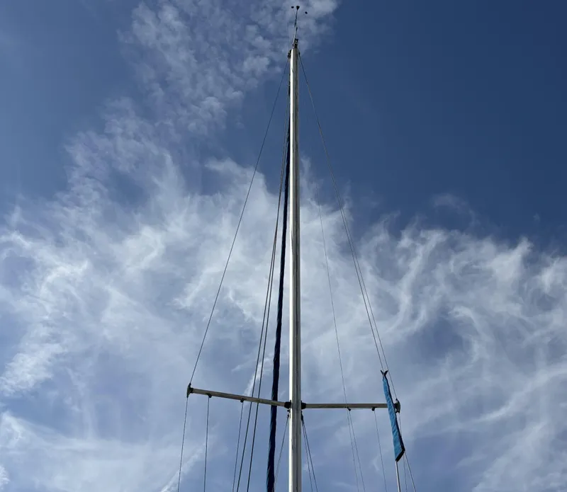Mast of 1985 Newport 30 sailboat against a blue sky with wispy clouds.