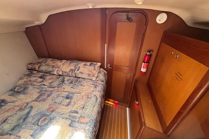 Cozy cabin interior of 1999 Hunter 410 sailboat with bed, wooden cabinetry, and fire extinguisher.