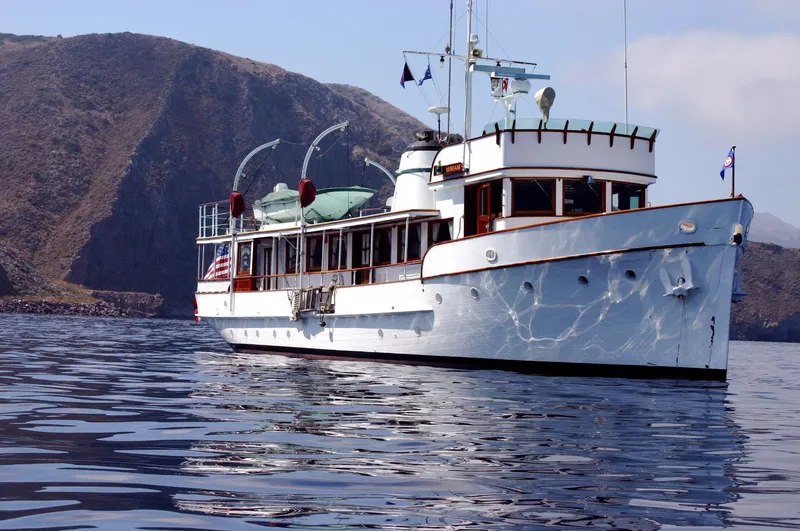 Classic 1946 J.M. Martinac yacht near rocky coastline.