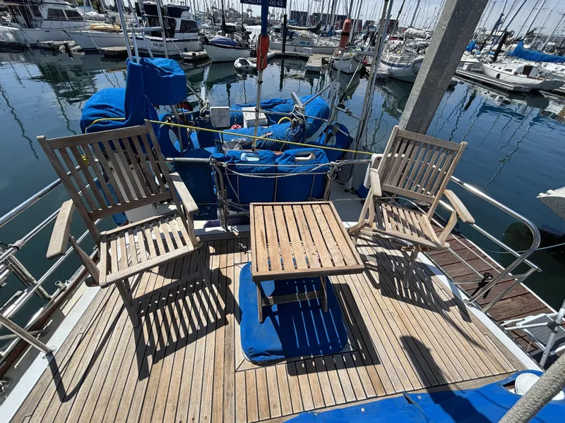 Wooden deck of 1973 CAL 246 sailboat with chairs and table in marina.