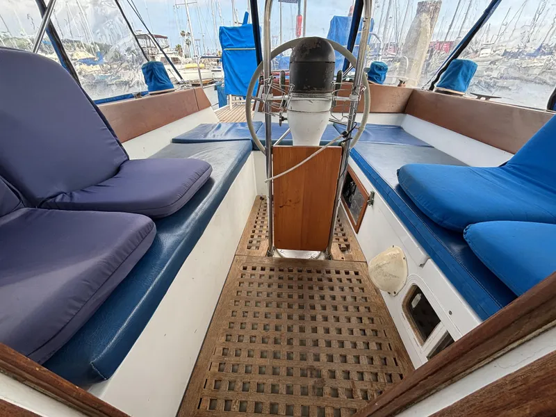 1973 CAL 246 sailboat cockpit with blue cushions and wooden flooring, docked at a marina.