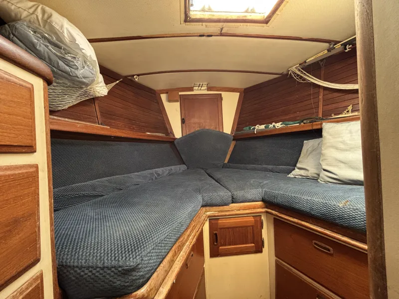 Cozy cabin interior of a 1973 CAL 246 sailboat with blue cushions and wooden accents.