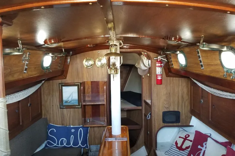Interior of 1977 Custom Bodega 30 sailboat with wooden decor and nautical-themed cushions.