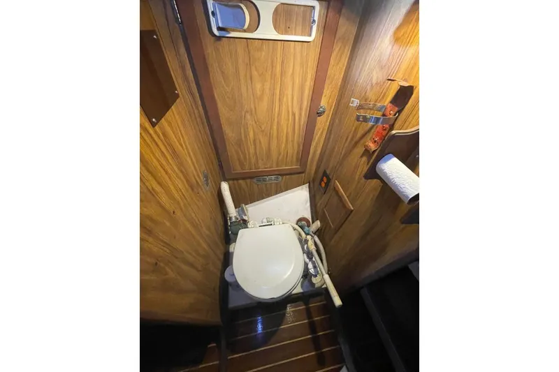 1977 Custom Bodega 30 boat bathroom with wooden paneling and compact toilet.