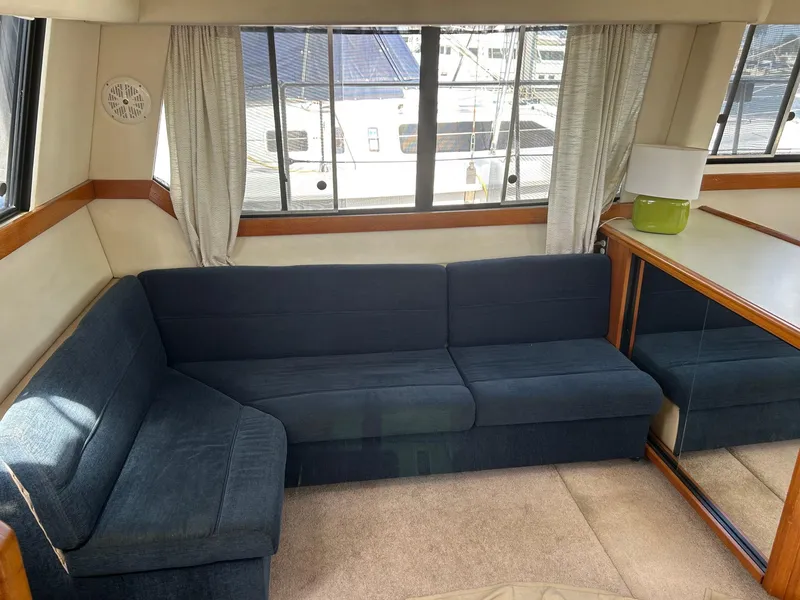 Interior of 1994 Bayliner 4587 Motoryacht with blue L-shaped sofa and large windows.