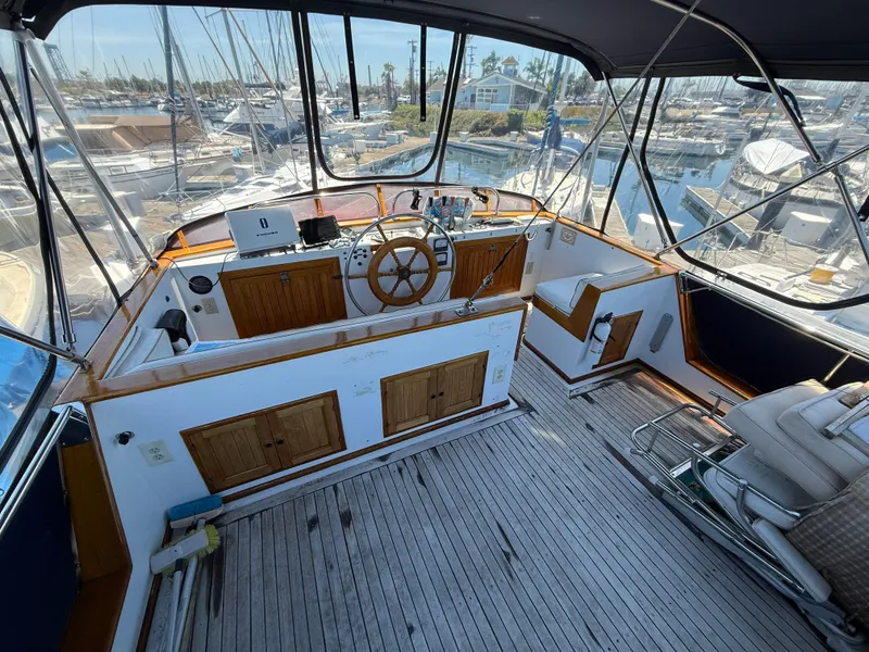 1981 DeFever Passagemaker yacht helm with wooden wheel and marina view.