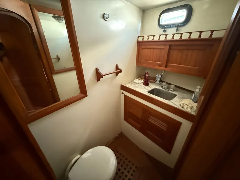 1981 DeFever Passagemaker bathroom with wooden cabinets, sink, and porthole window.