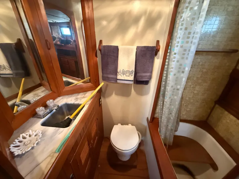 1981 DeFever Passagemaker bathroom with sink, toilet, and shower, featuring wooden cabinetry.