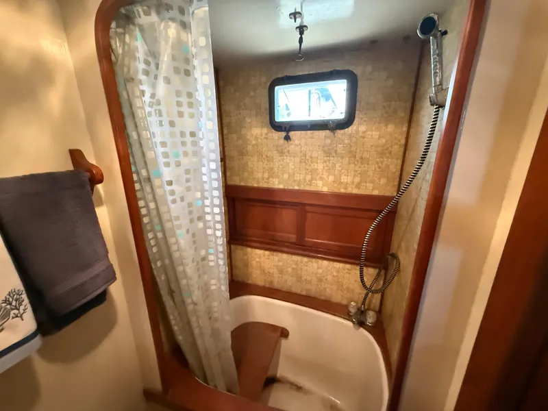 1981 DeFever Passagemaker bathroom with shower, wooden accents, and porthole window.