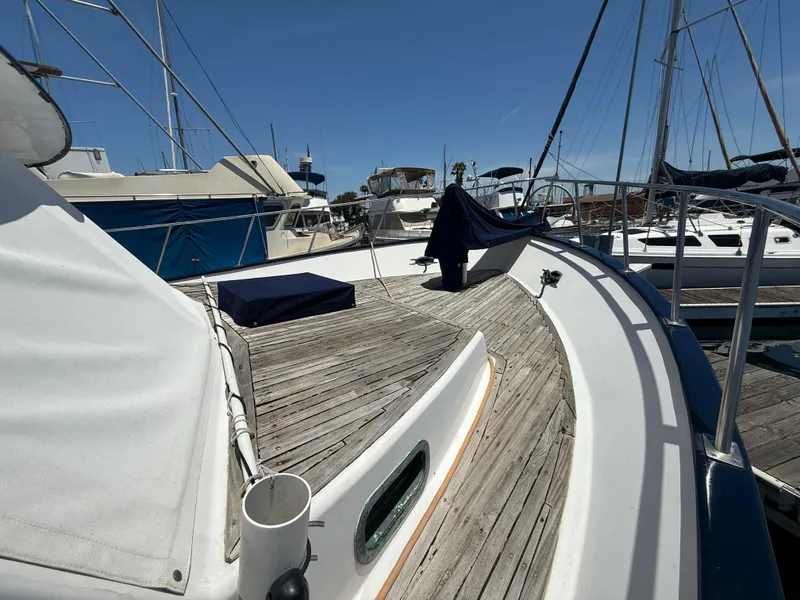 1981 DeFever Passagemaker yacht with wooden deck, docked in a marina under clear skies.