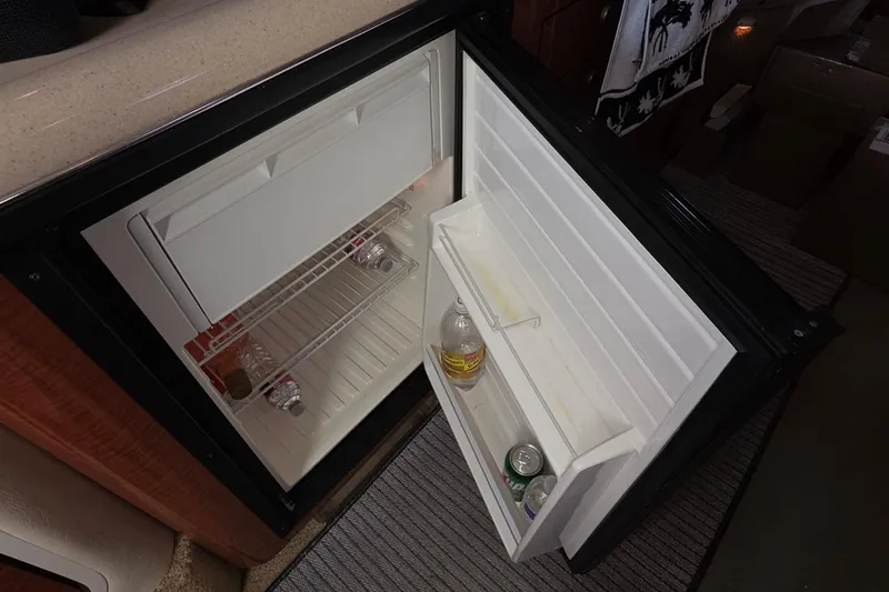 Open mini fridge inside 2005 Sea Ray 340 Sundancer boat, containing drinks and bottles.