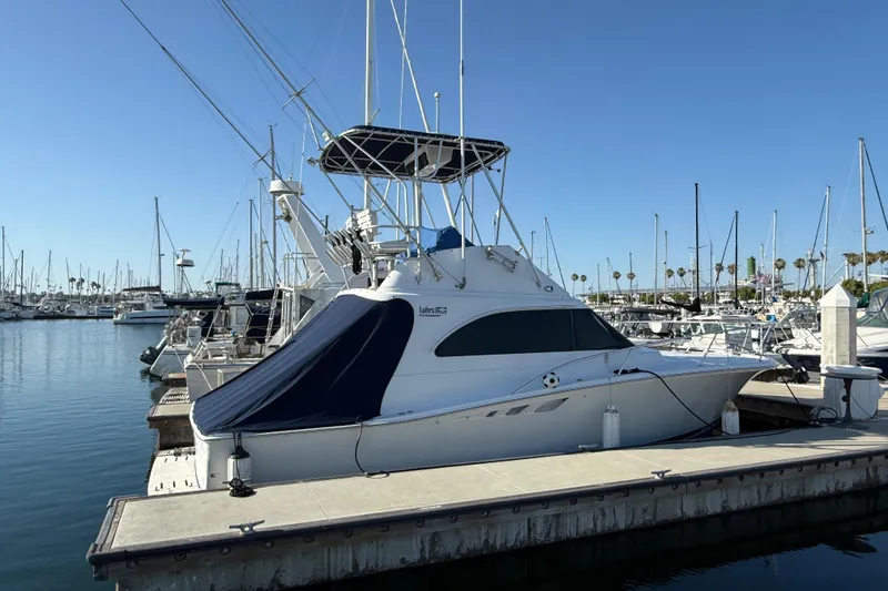 1998 Luhrs Tournament 320 Convertible yacht docked at a marina under clear blue skies.