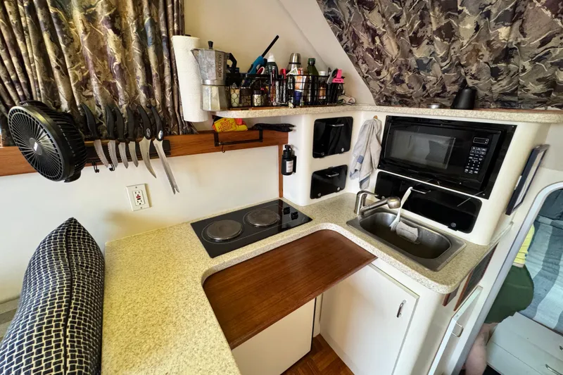 Compact kitchen in a 1998 Luhrs Tournament 320 Convertible boat, featuring stove, sink, and microwave.