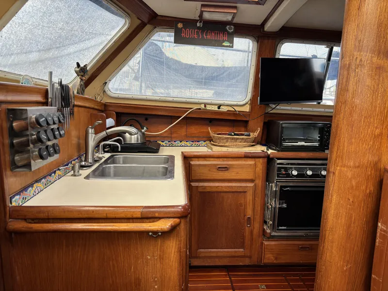 1973 CAL 246 yacht kitchen with wooden cabinetry, sink, stove, and TV.