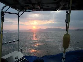 Sunset view from a 1973 CAL 246 boat, overlooking calm waters and distant hills.