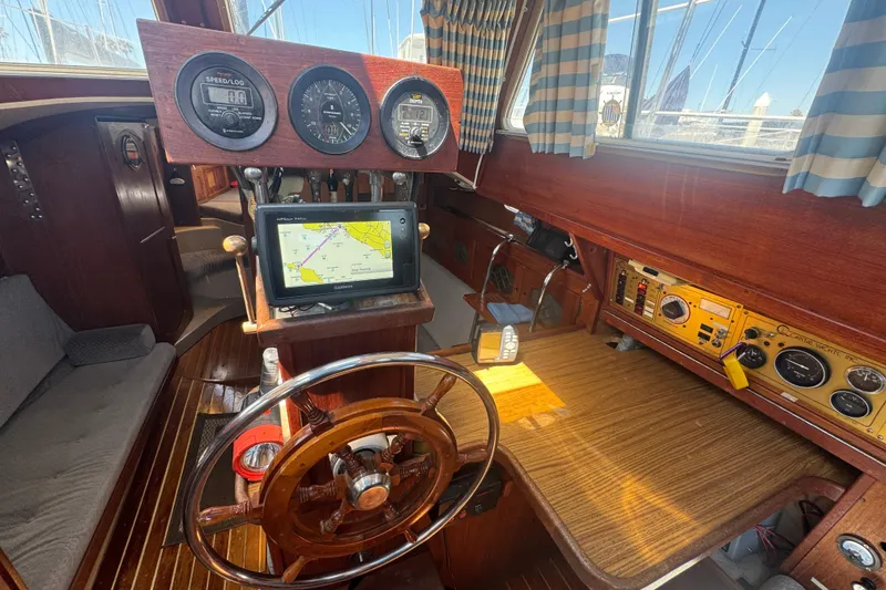 1988 Gulf Pilot House interior with wooden steering wheel, navigation instruments, and striped curtains.