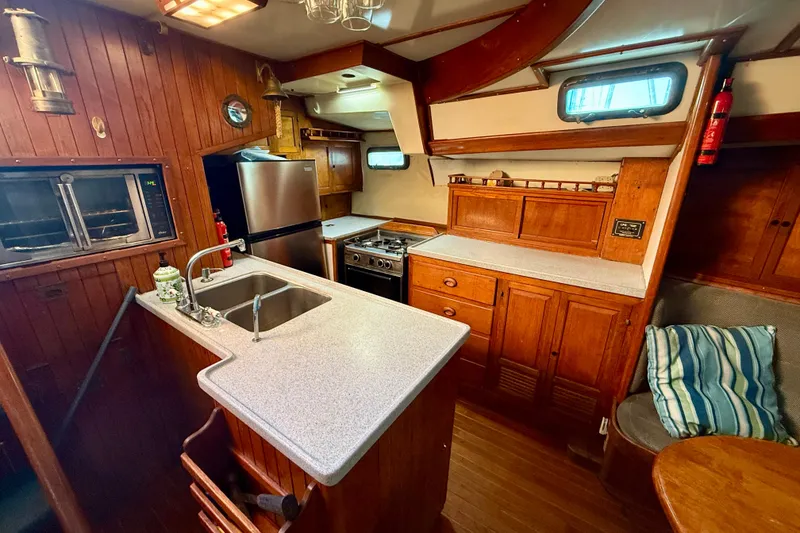 1981 Mariner Mayflower yacht kitchen with wooden cabinetry, stainless steel appliances, and cozy seating area.
